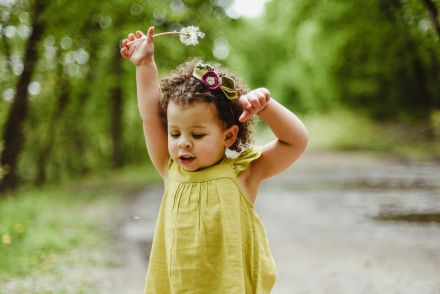 Adorable young girl playing in a lush green forest on a bright spring day.