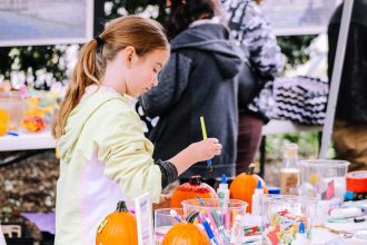 A child enjoys painting pumpkins at an outdoor crafting event, surrounded by art supplies.